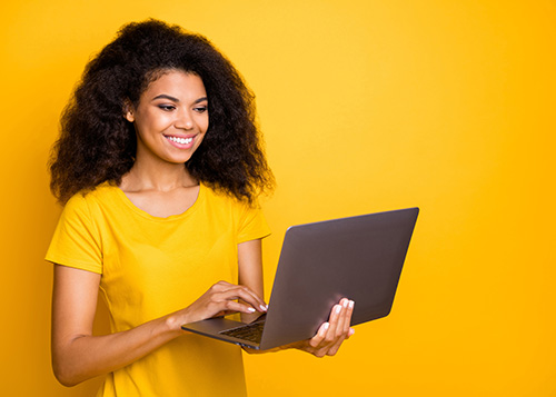 women in yellow tshirt and yellow background smiling holding laptop